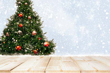 Top of empty wood table with beautiful Christmas tree and snowfall  backdrop. ready for your product display or montage. Concept of background in Christmas and New year holidays.