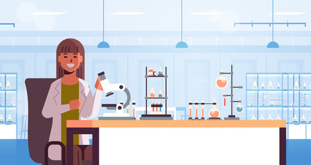 scientist using microscope and test tubes woman in uniform sitting at table making scientific experiments chemistry laboratory interior research science concept horizontal portrait