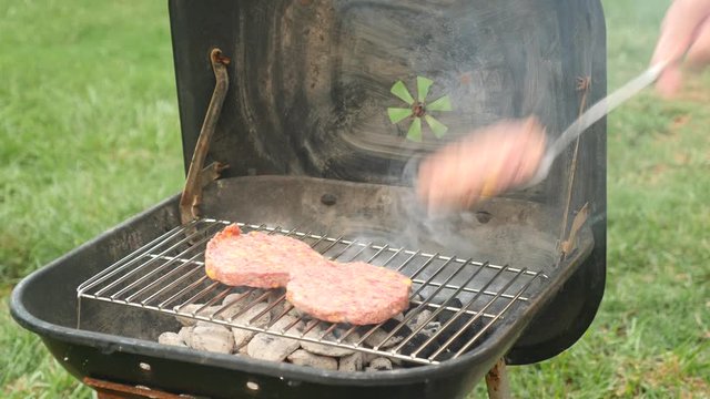 Raw hamburger patties cook on a charcoal grill during a summer cookout