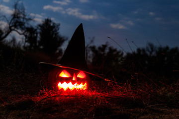 Spooky Halloween pumpkin jack-o-lantern in witch hat with burning candles in scary forest at night