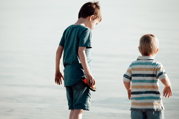 two young brothers or children at the beach looking at the water, back to camera