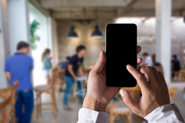 Hand holding black phone with a blank screen in the cafe in the morning light.