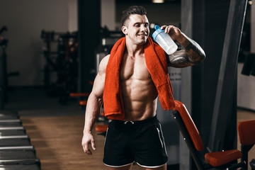 Fototapeta na wymiar Muscular tattoo man bodybuilder training in gym and posing. Fit muscle guy drinking water after workout with weights and barbell