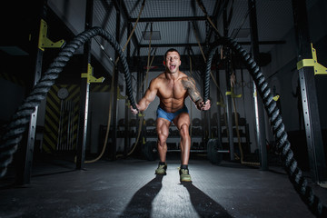 Naklejka na ściany i meble Athletic pumped man bodybuilder is engaged with ropes in hall of crossfit
