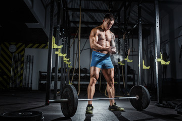 Fototapeta na wymiar Athletic pumped man bodybuilder stands in front of bar in gym