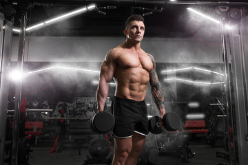 Fototapeta na wymiar Bodybuilder professional athlete man posing with dumbbells in gym