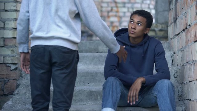 Young man stretching out hand to sad friends sitting stairs, friendship support