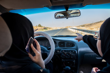 Two arabic women driving a car while one is talking on the phone