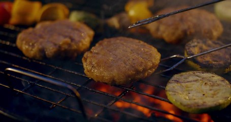 EXTREME CU Cooking vegetarian alternative burger meat with vegetables on a flaming grill during outdoor barbecue party. 4K UHD
