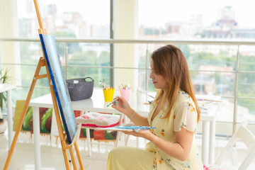 Art class, drawing and creativity concept - Female student sitting in front of easel with palette and paintbrush