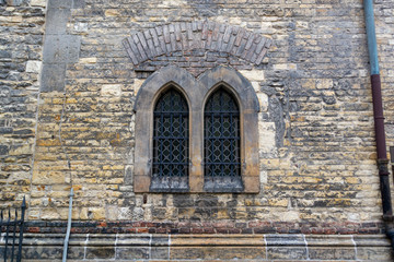 Wall of old masonry with blackened stones and two windows in the Gothic style