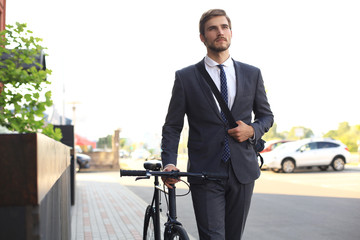 Fototapeta na wymiar Pensive young businessman walking with bicycle on the street in city.