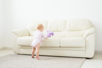 childhood, babyhood and people concept - happy little baby girl playing near couch at home