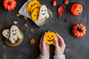 Female hands holding  pumpkin scary face cookie on dark background with halloween symbol sand decoration. Happy Halloween concept.