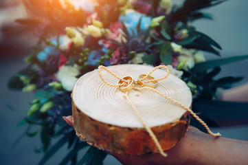 Bride holds wooden stand with golden wedding rings. A touching moment at the ceremony. Rings on round wooden stand, close up.