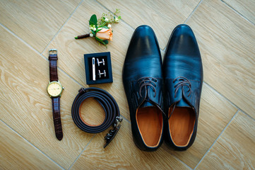 Men's shoes in black leather, close-up. Wedding concept. Men's shoes, cufflinks, belt, watch and boutonniere, top view.