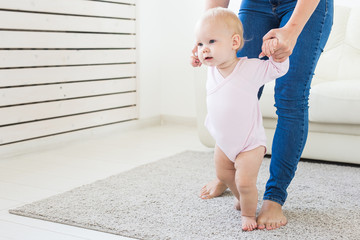 First steps of baby toddler learning to walk in white sunny living room. Footwear for child.