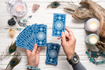 Fortune teller woman and a blue tarot cards over white wooden table background. - obrazy, fototapety, plakaty
