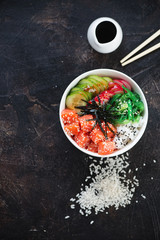 Poke bowl with salmon, flatlay over dark brown stone background, vertical shot with copy space