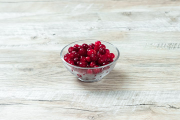 Red cranberries in a glass bowl on a white wooden background