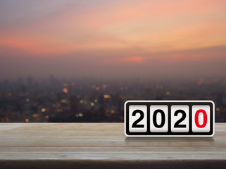 Retro flip clock with 2020 text on wooden table over blur of cityscape on warm light sundown, Happy...