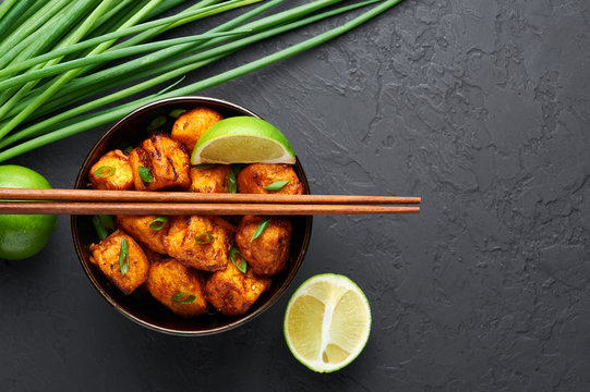 Paneer Manchurian or Paneer 65 in bowl at black concrete background. Paneer Manchurian is Indian Chinese cuisine dish with panner cheese, tomatoes, onion, soy sauce. Copy space
