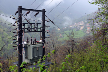 High-voltage substation transformer on mountains and fog clouds background.