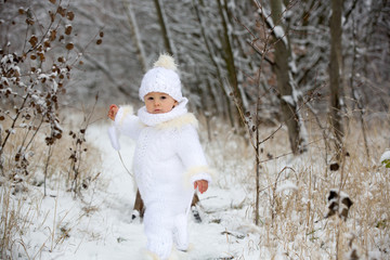 Cute little toddler boy and his older brothers, playing outdoors with snow on a winter day