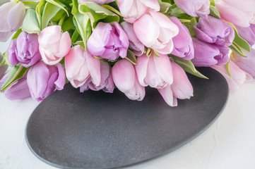 Fototapeta na wymiar Beautiful bouquet of purple and pink tulips lying on a black decorative plate. Copy space. Congratulation.