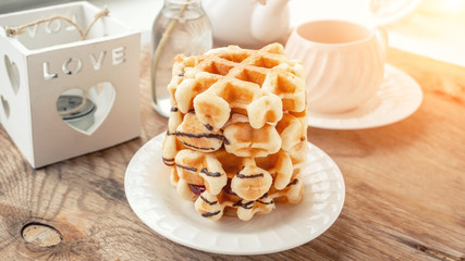 Delicious Fresh round Belgian waffles with a layer of jam poured chocolate on a white plate with a Cup of tea. Close up