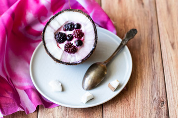 Berry dessert with yogurt in a cup of coconut on a wooden background. Blackberries, raspberries, blueberries, black currants.