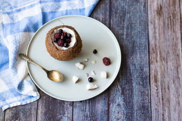 Berry dessert with yogurt in a cup of coconut on a wooden background. Blackberries, raspberries, blueberries, black currants.