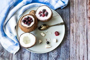 Berry dessert with yogurt in a cup of coconut on a wooden background. Blackberries, raspberries, blueberries, black currants. Blue napkin