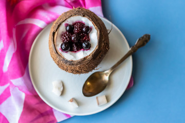 Berry dessert with yogurt in a cup of coconut on a blue background. Blackberries, raspberries, blueberries, black currants. Pink napkin