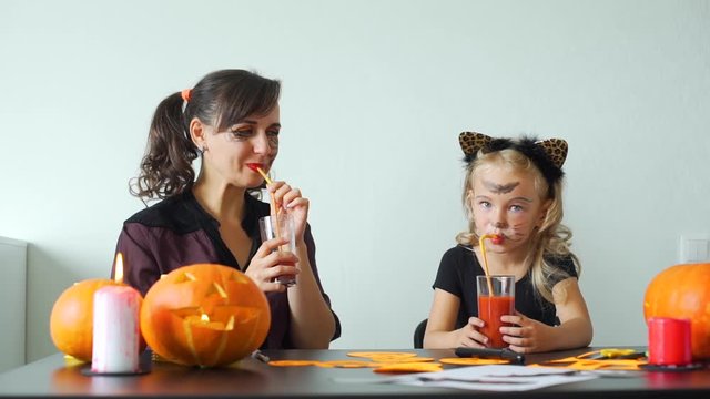 Little Girl and her Mother Drinking Tomato Juice while Making Decorations for Halloween Party. Halloween Holiday Concept