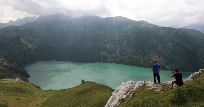 Young travellers take a photo with the stunning background of Ritom Lake in the Swiss Alps in slow motion