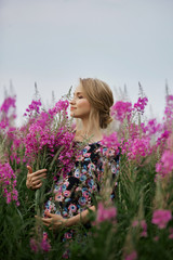 Fototapeta premium Pregnant girl walking in field of flowers fireweed, woman smiling and picking flowers. The girl is expecting the birth of a baby in the ninth month of pregnancy