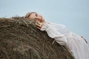 Pregnant girl walks in a field near haystacks in a long white dress, a woman smiles and holds her...