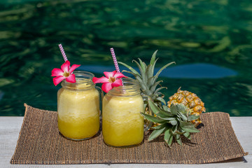 Homemade mango and pineapple smoothie made with coconut milk in two glass mug near swimming pool . Island Bali, Indonesia. Refreshing tropical fruit drink