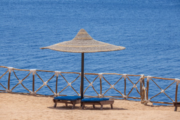Fototapeta premium Straw umbrellas with wooden sun loungers next to the red sea on sand beach at the resort in Sharm El Sheikh, Egypt
