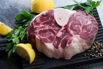 Close-up of raw cross cut veal shank for making osso buco with lemon, parsley and spices, studio shot