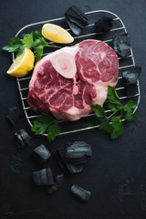Fresh uncooked cross cut veal shank for making osso buco, above view on a black stone background with charcoals