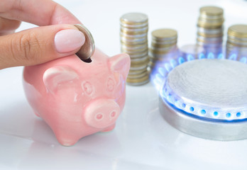 Female hand with coin and piggy bank near the flame of a gas stove in the kitchen. Symbolic image...