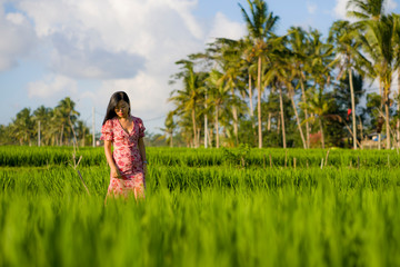 natural and fresh lifestyle portrait of  young beautiful and attractive Asian Korean woman in elegant dress walking on green rice field enjoying exotic Summer holidays