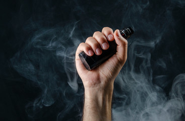 hand holding vape e-cigarette or electronic cigarette with white smoke over a black background. 