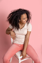 Freestyle. African girl sitting on chair isolated on pink laughing joyful top view