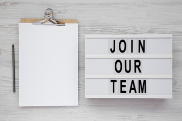 'Join our team' words on a lightbox, clipboard with blank sheet of paper on a white wooden...