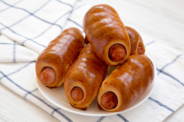 Homemade beef sausage kolache on a white plate on a white wooden background, side view. Close-up.