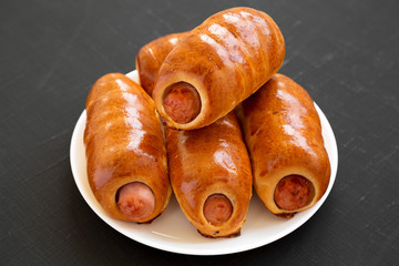 Homemade beef sausage kolache on a white plate on a black surface, side view. Close-up.