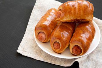 Homemade beef sausage kolache on a white plate on a black background, side view. Copy space.